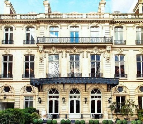 The stone facade of a Parisian townhouse, with wrought-iron balconies and arched ground-floor windows